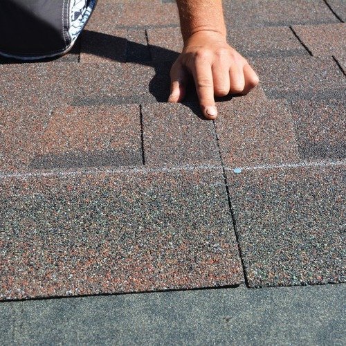close-up of a roofer placing down asphalt shingle roofing